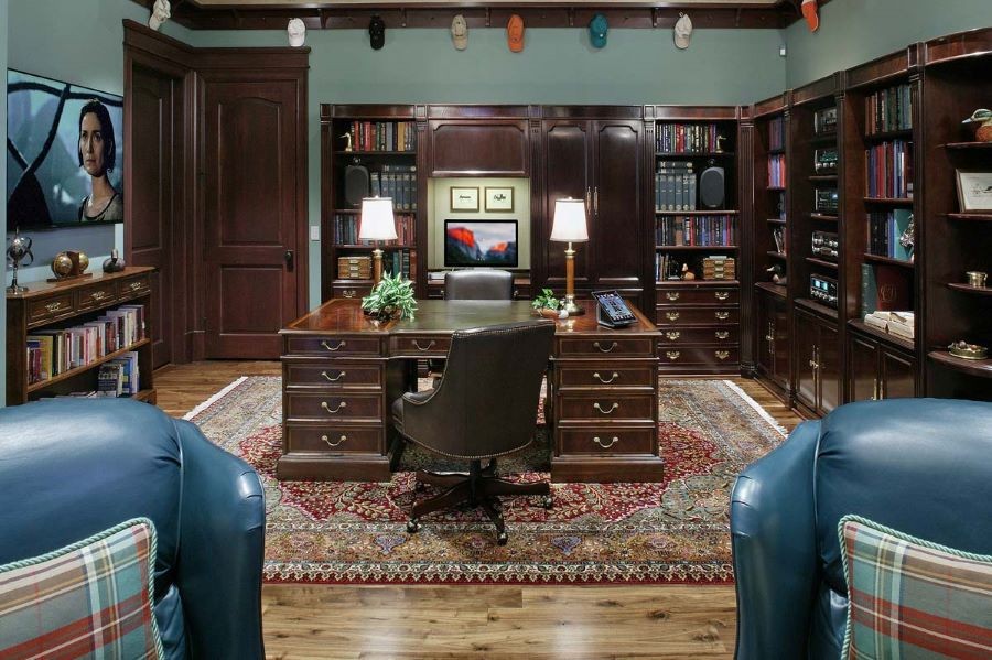 A home office with bookshelves lining the walls, a control touchscreen on the desk, and a TV.